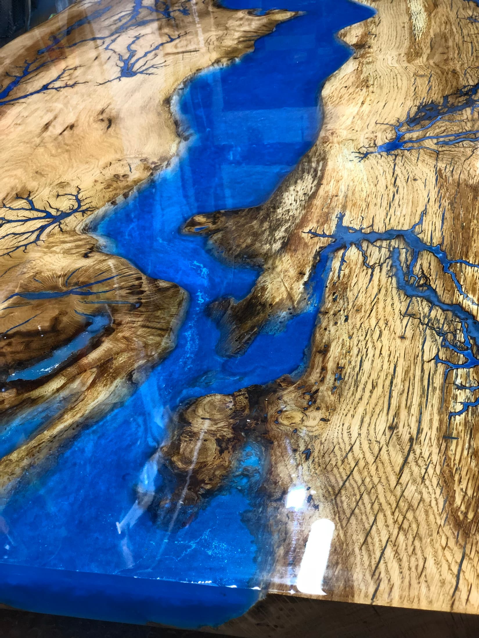 Close detail of a blue resin river with Lichtenberg branching through timber grain