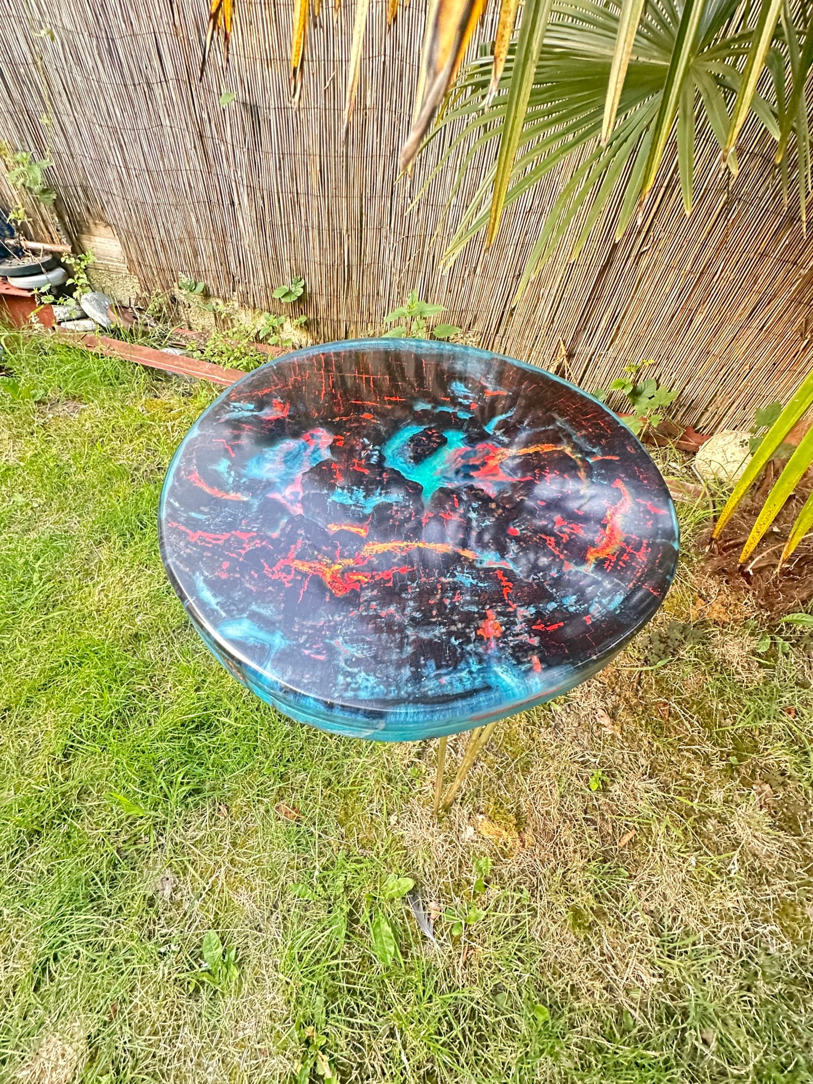 Round table with a charred timber top filled with red, orange and blue resin, outdoors