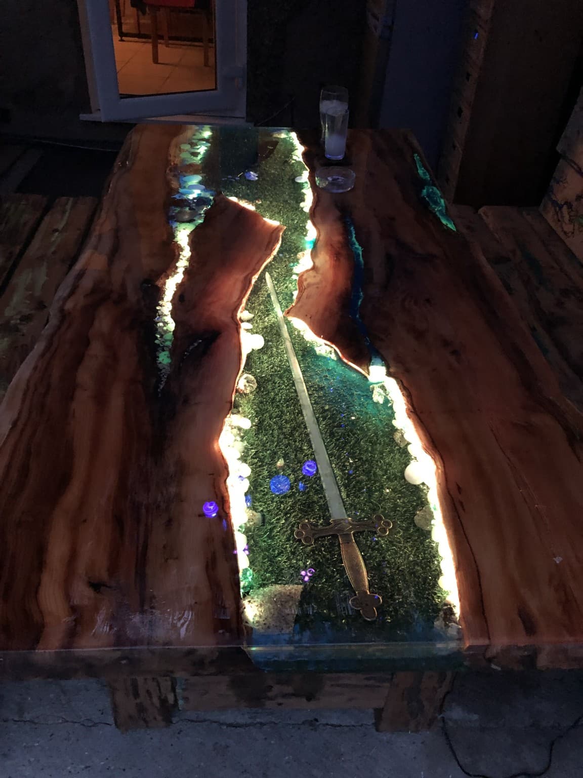 Live-edge table with a full sword laid across a glowing green moss-and-resin river