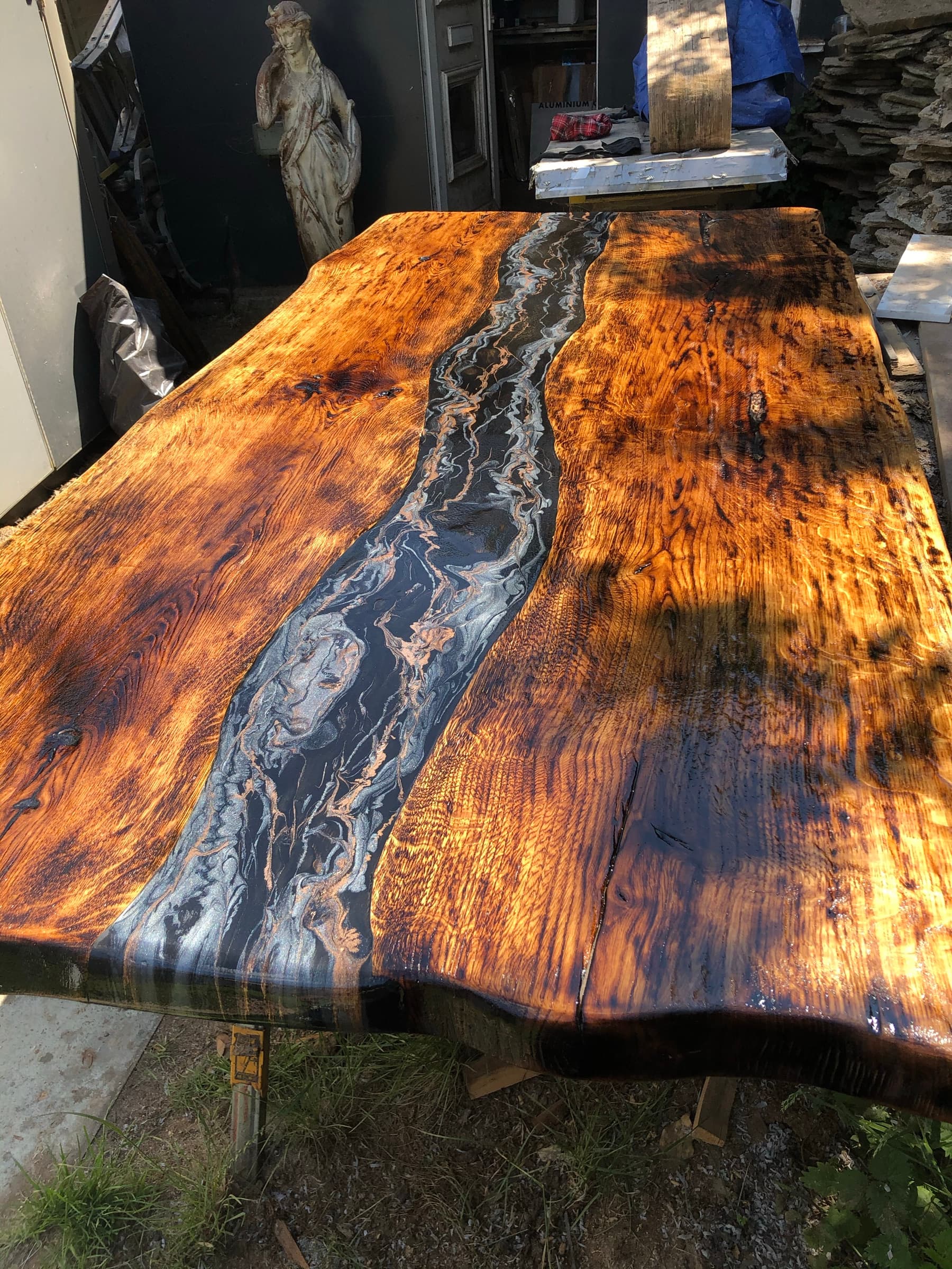 The finished charred tabletop with a black and gold marbled river, outdoors on its leg base