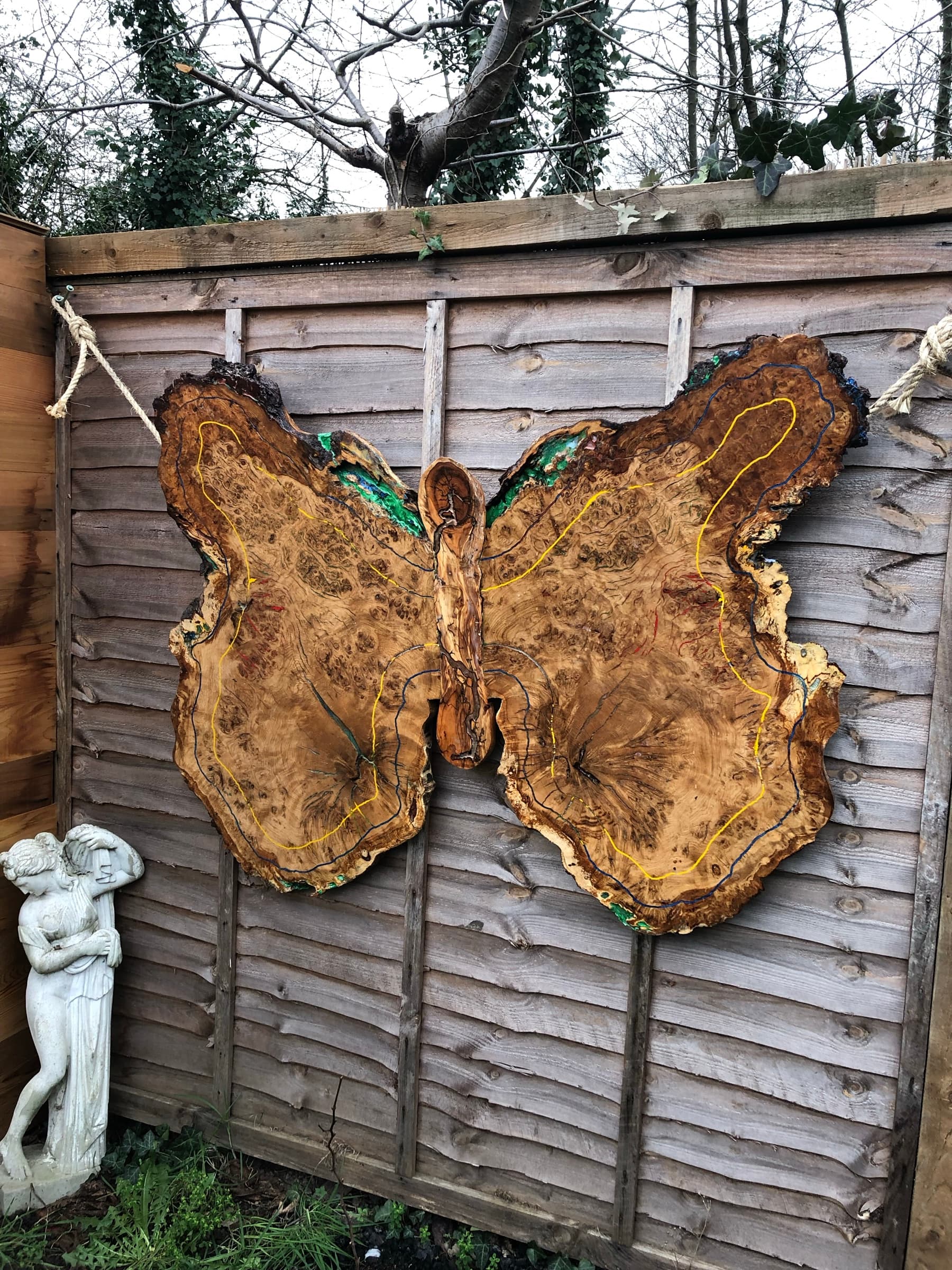The finished Butterfly piece hung by rope on an outdoor fence, full wingspan visible