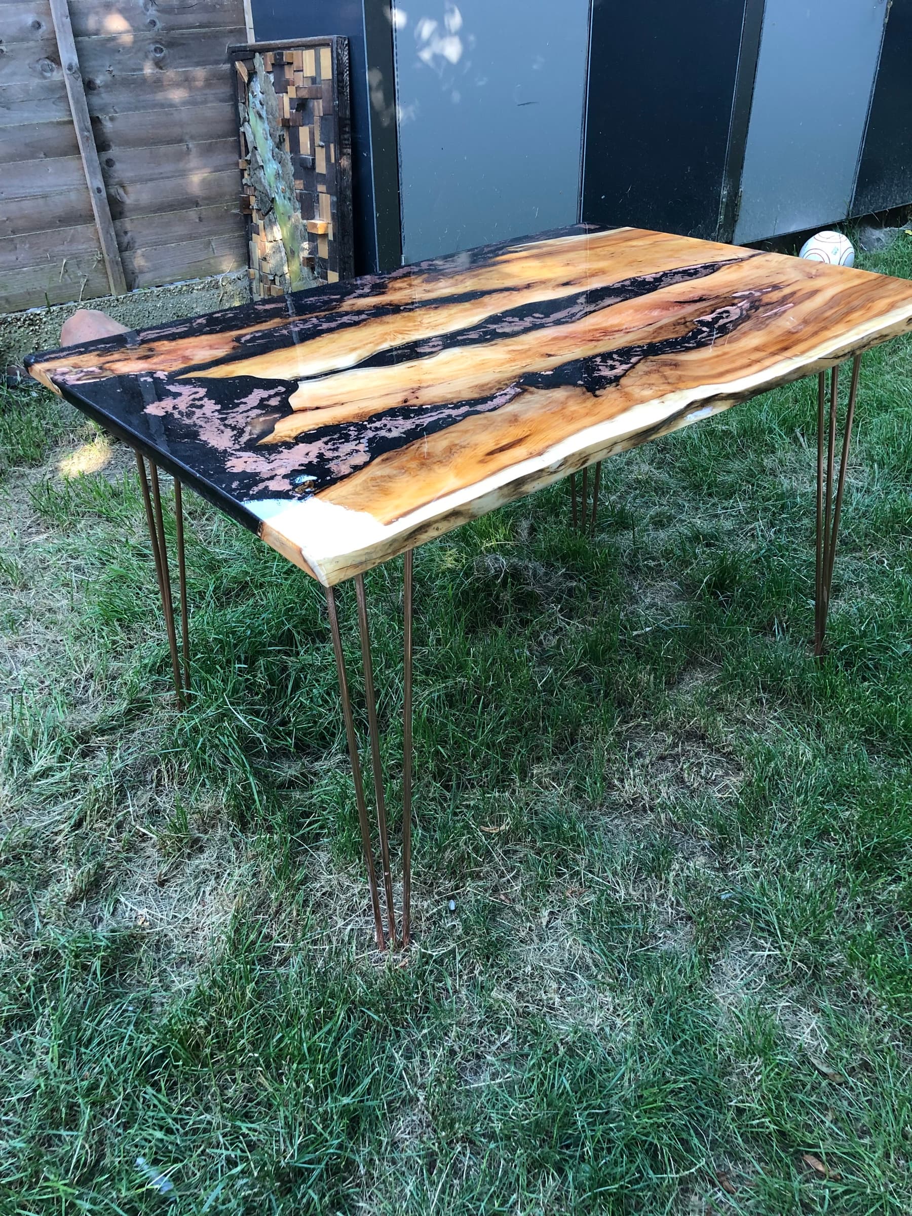 The finished live-edge yew table on copper-toned hairpin legs, outdoors in a garden