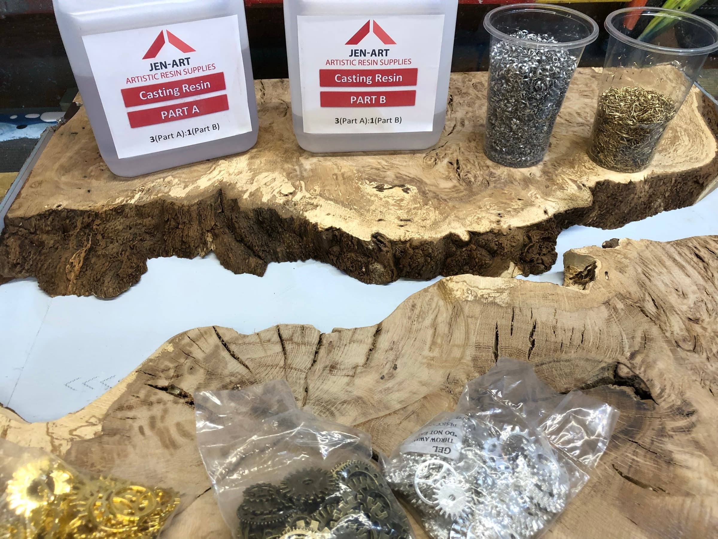 Casting resin and cups of metal shavings and gears laid out on the raw burl slabs, workshop