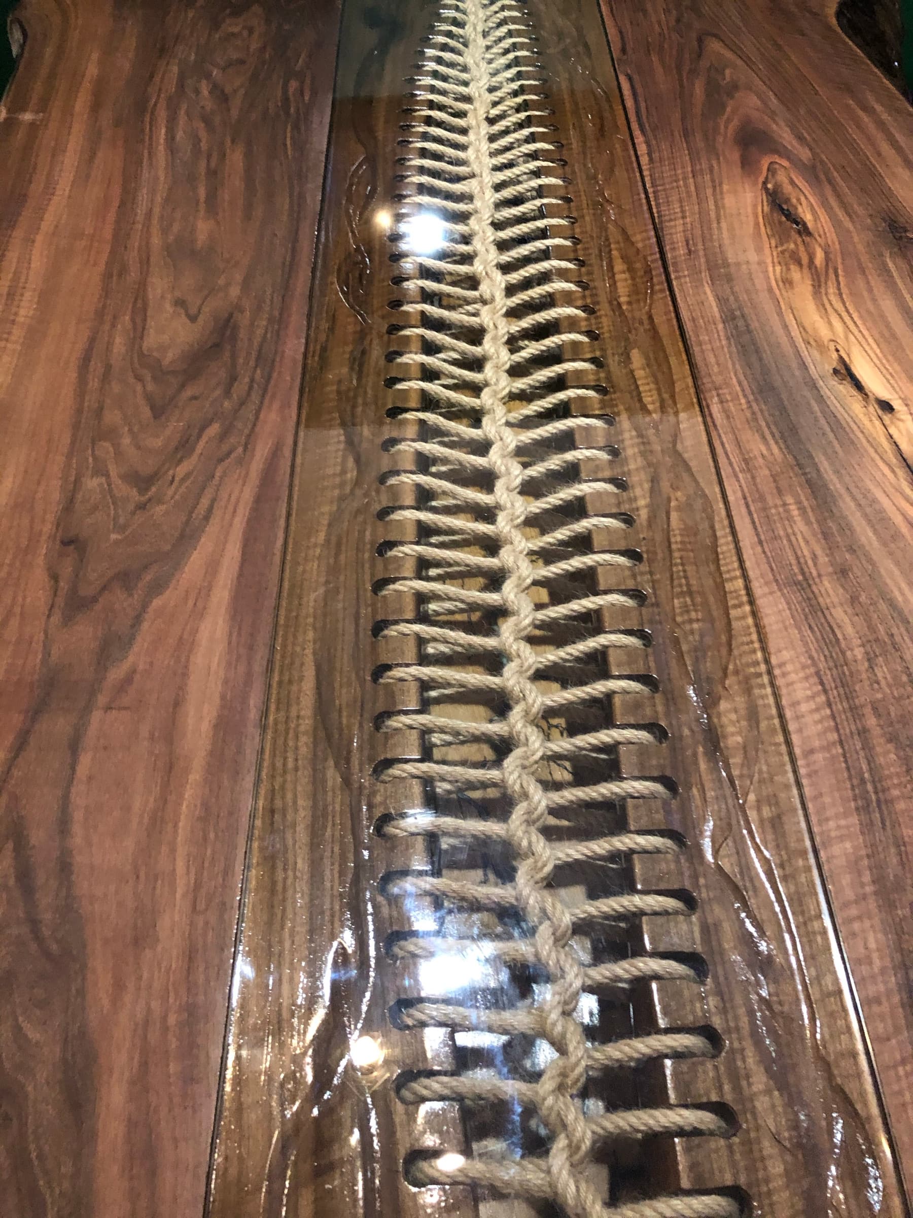 Macro detail of the hand-laced rope spine beneath a glossy clear channel, walnut grain either side