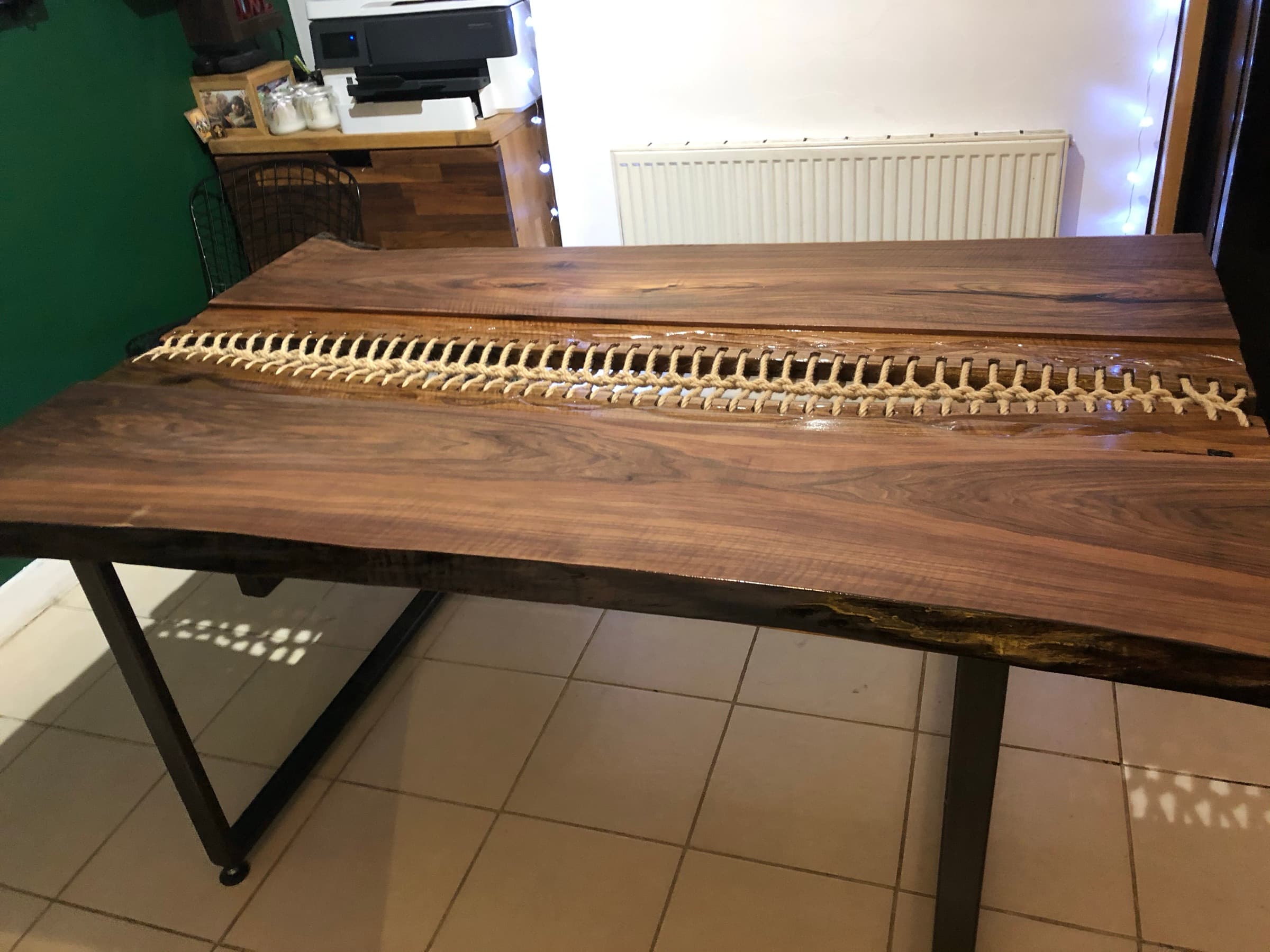 Walnut dining table with a rope-laced centre seam on black steel legs, indoor