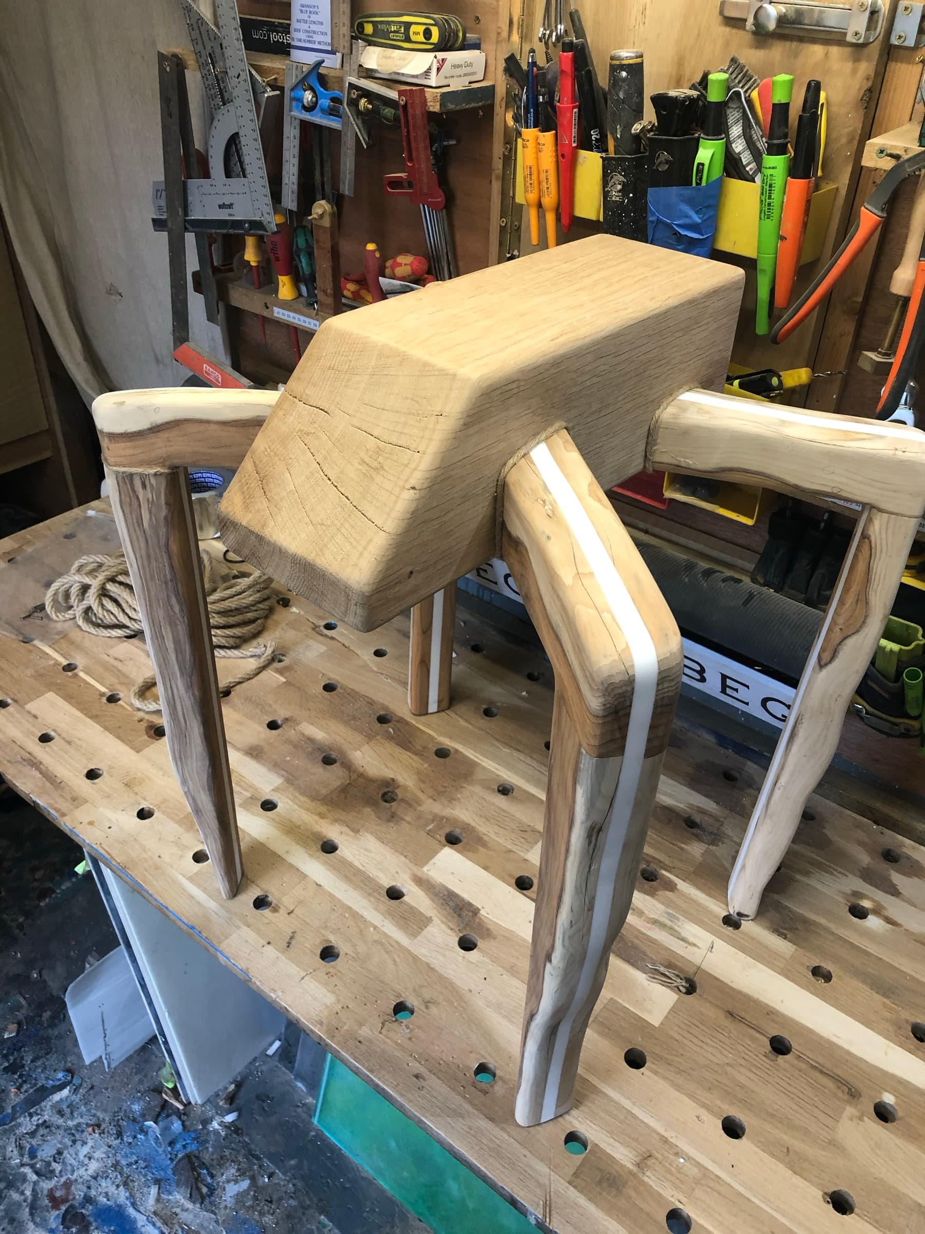 The carved legs joined to the raw top block early in construction, workshop pegboard behind