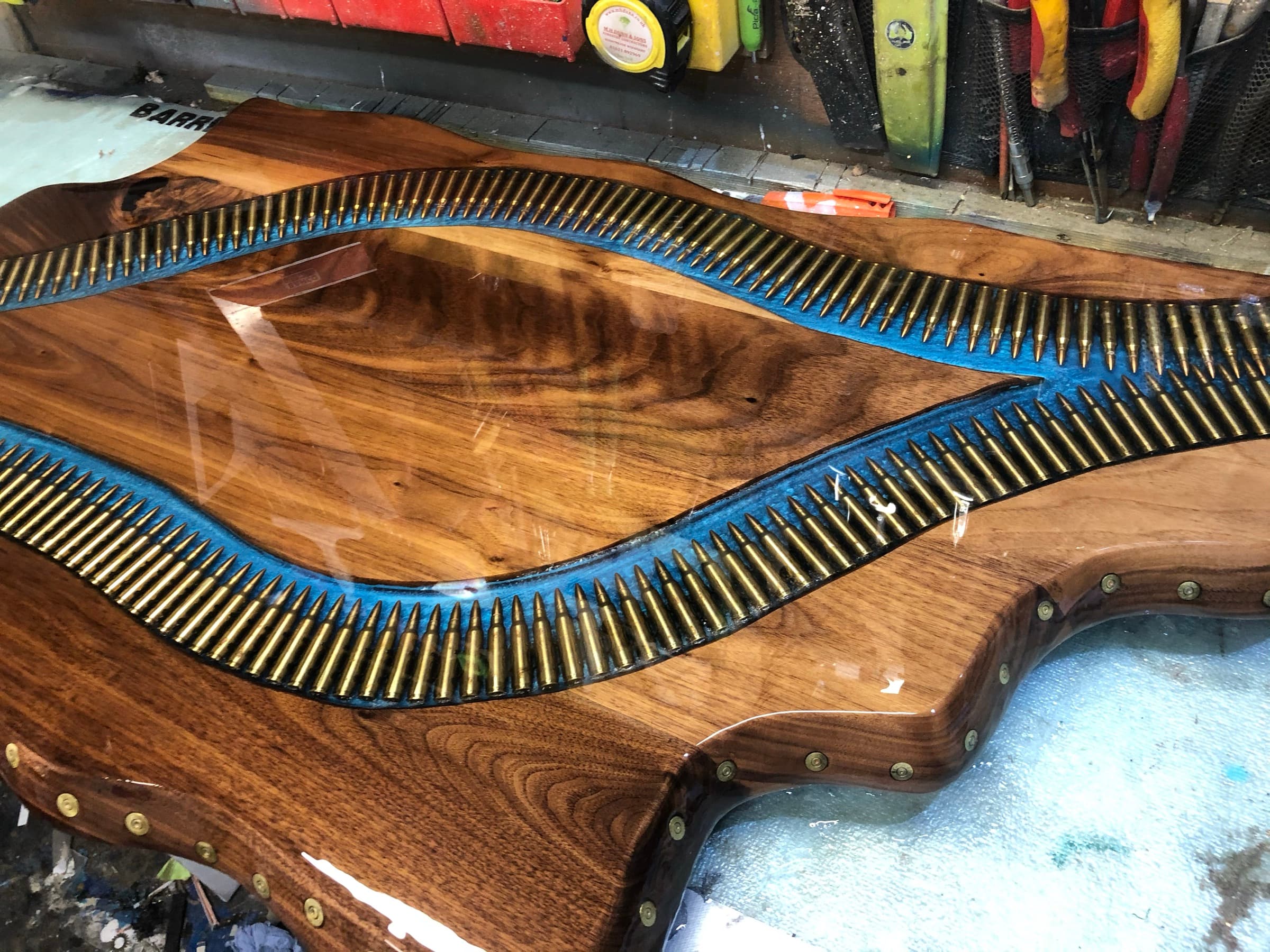 Walnut tabletop with an S-curved river of brass cartridge casings set in blue resin, scalloped live edge