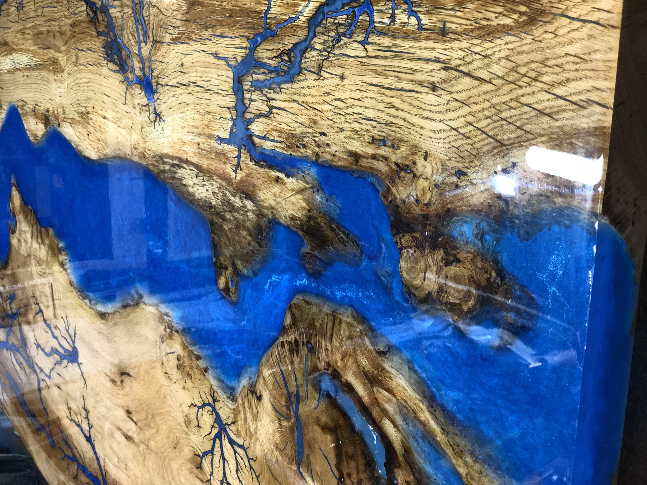 Close detail of a blue resin river with Lichtenberg branching through timber grain