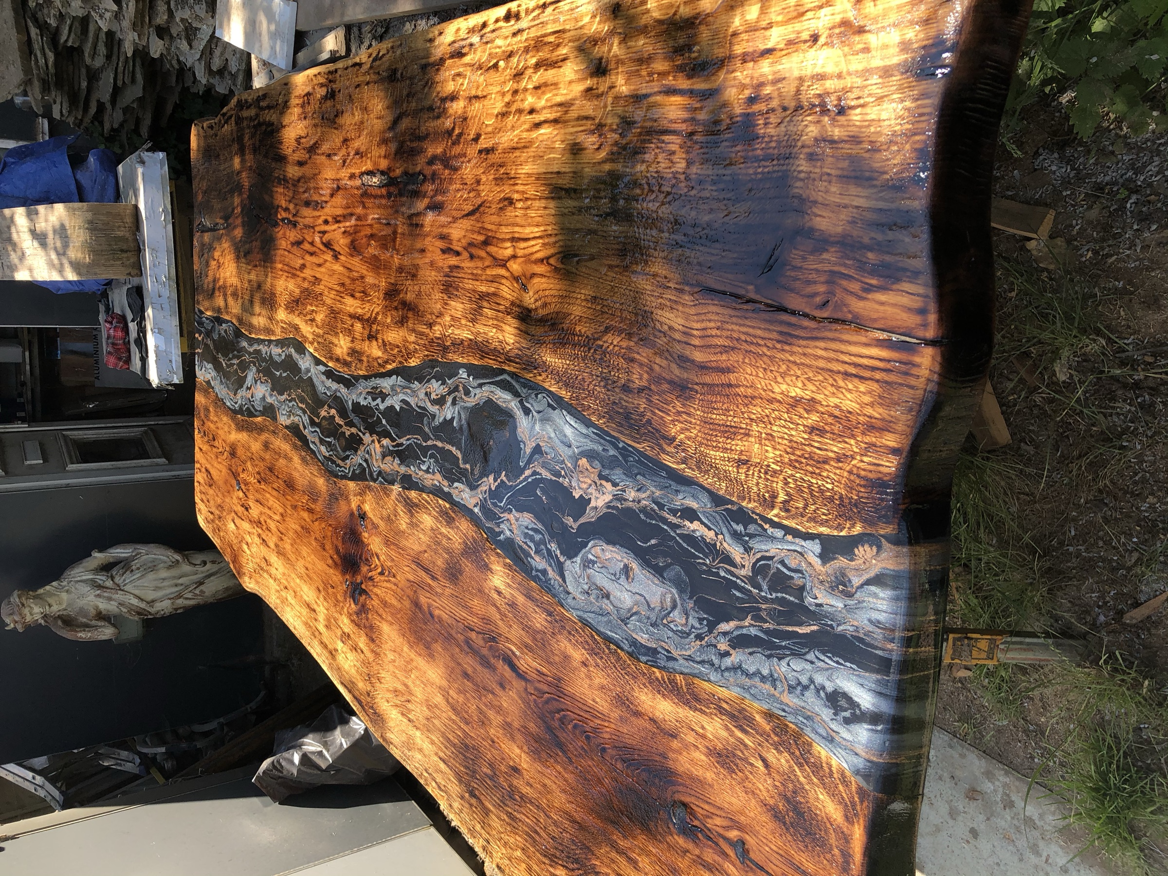 The finished charred tabletop with a black and gold marbled river, outdoors on its leg base