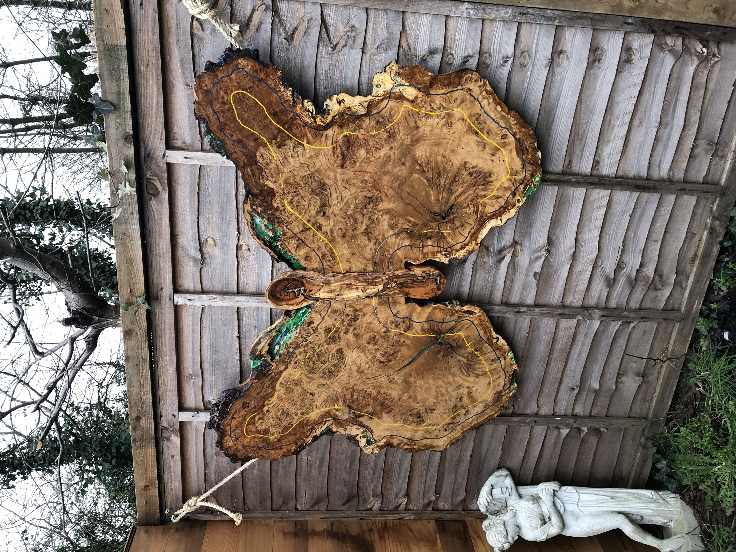 The finished Butterfly piece hung by rope on an outdoor fence, full wingspan visible