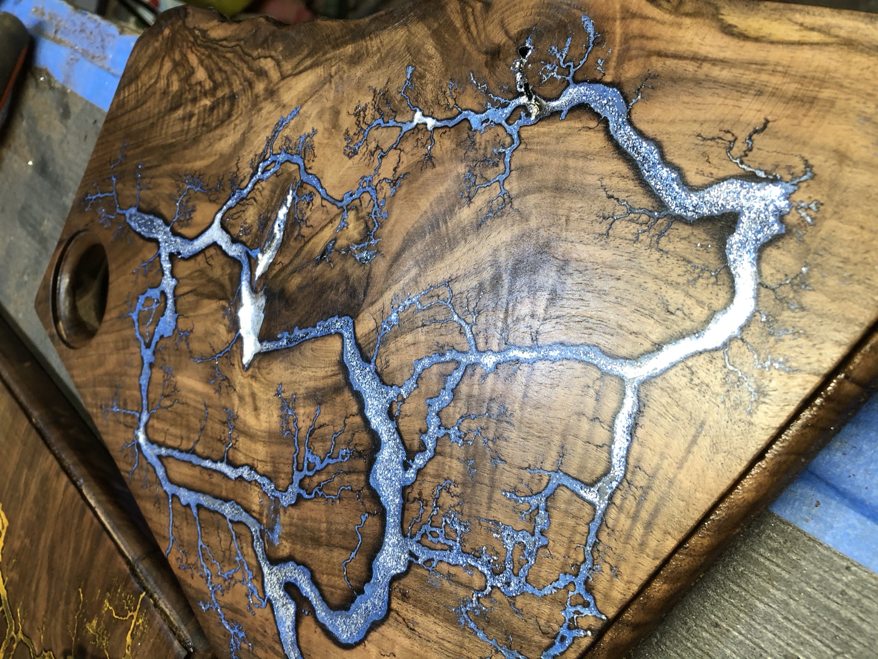 Macro detail of silver Lichtenberg branching filled with metallic pigment across a walnut board