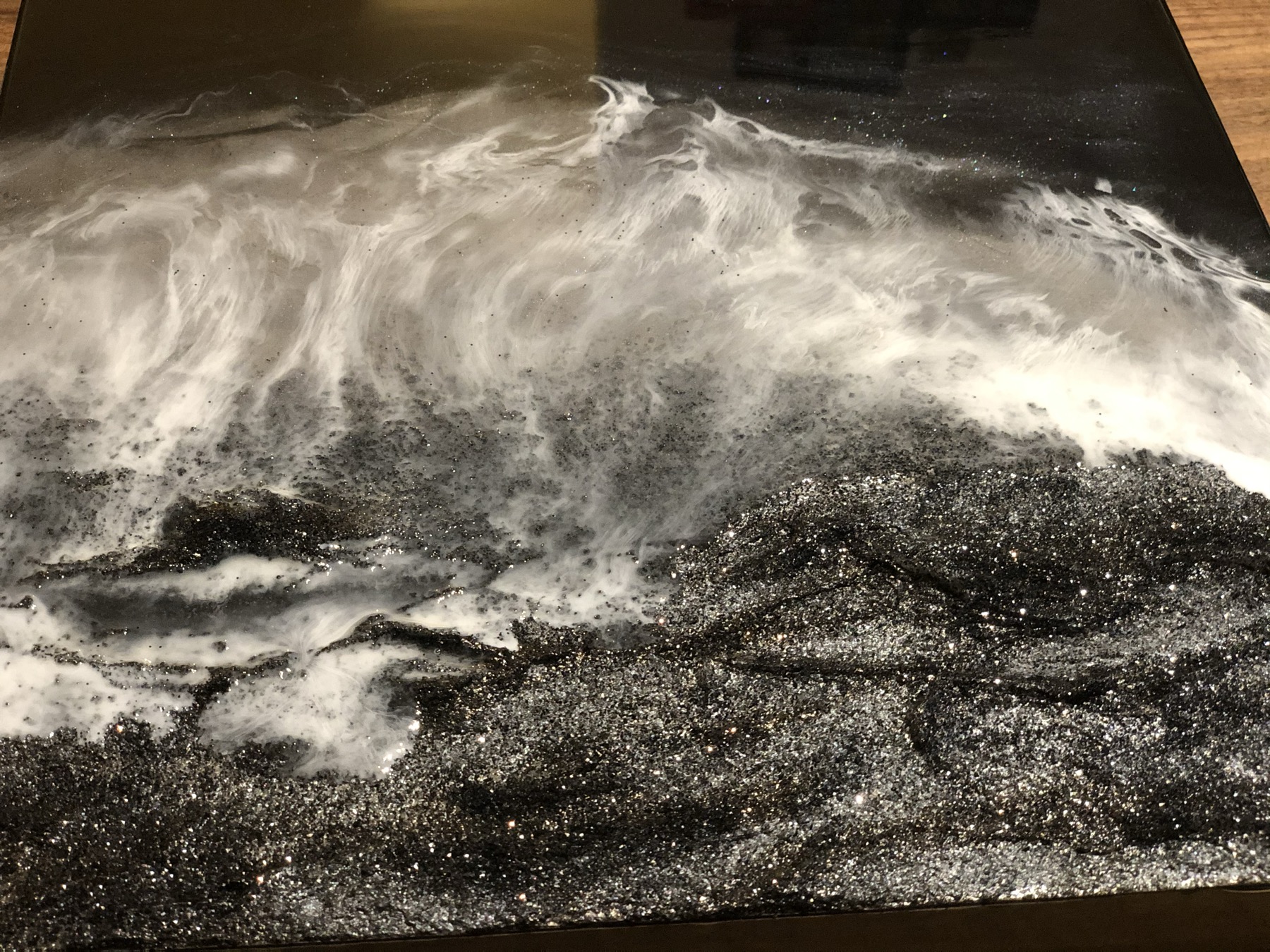 Close detail of a black, white and glitter resin surface poured in a wave pattern