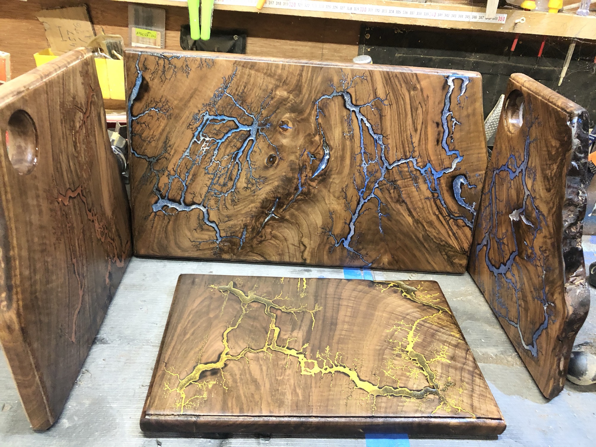Several finished boards standing together in the workshop, silver and gold Lichtenberg branching through walnut grain