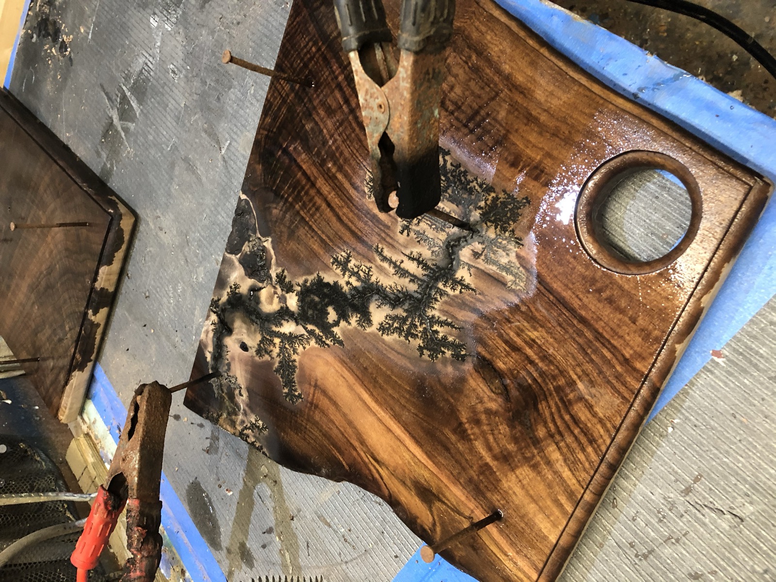 A board clamped to the workbench mid-burn on the Lichtenberg fractal-branching rig