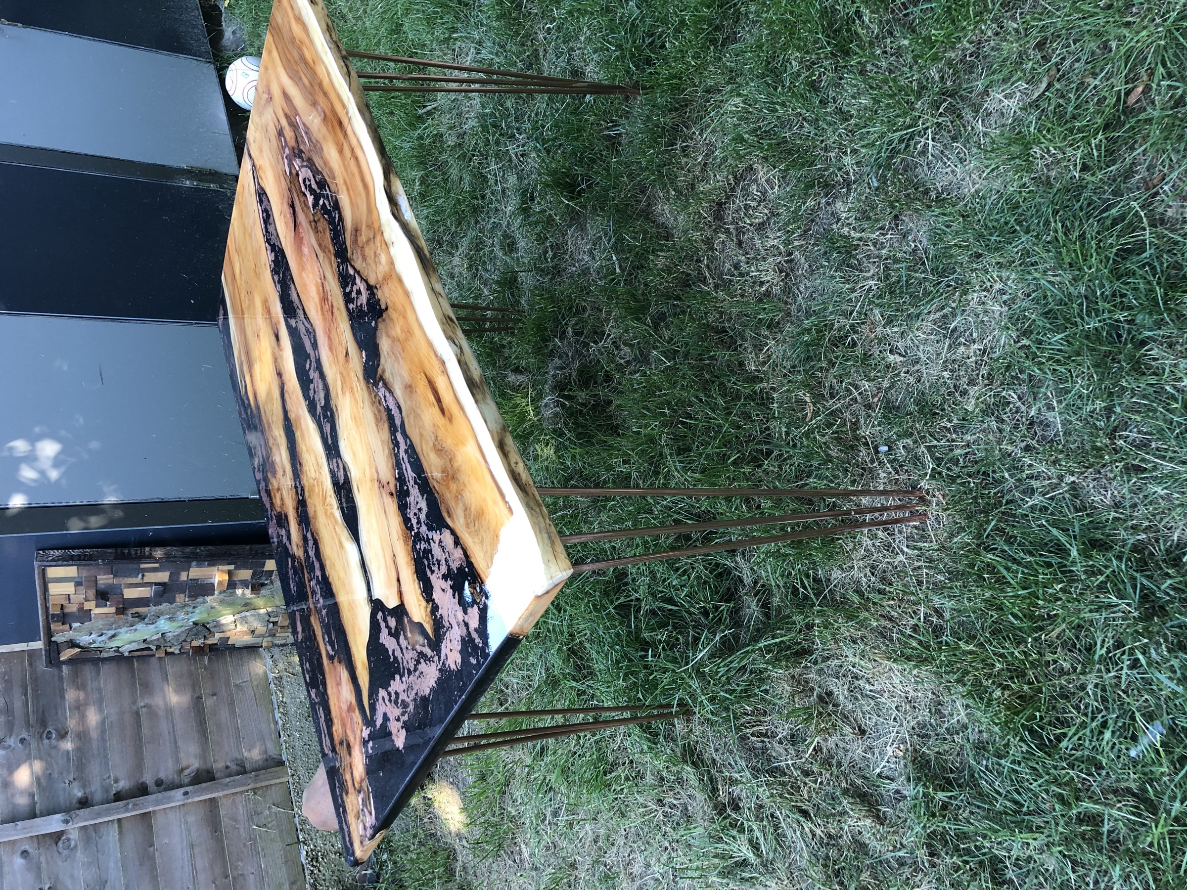 The finished live-edge yew table on copper-toned hairpin legs, outdoors in a garden