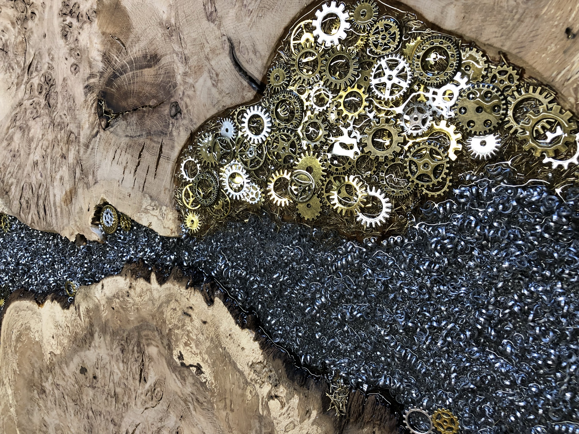 Macro detail of steel shavings flowing into a cluster of brass and steel watch gears, set in resin