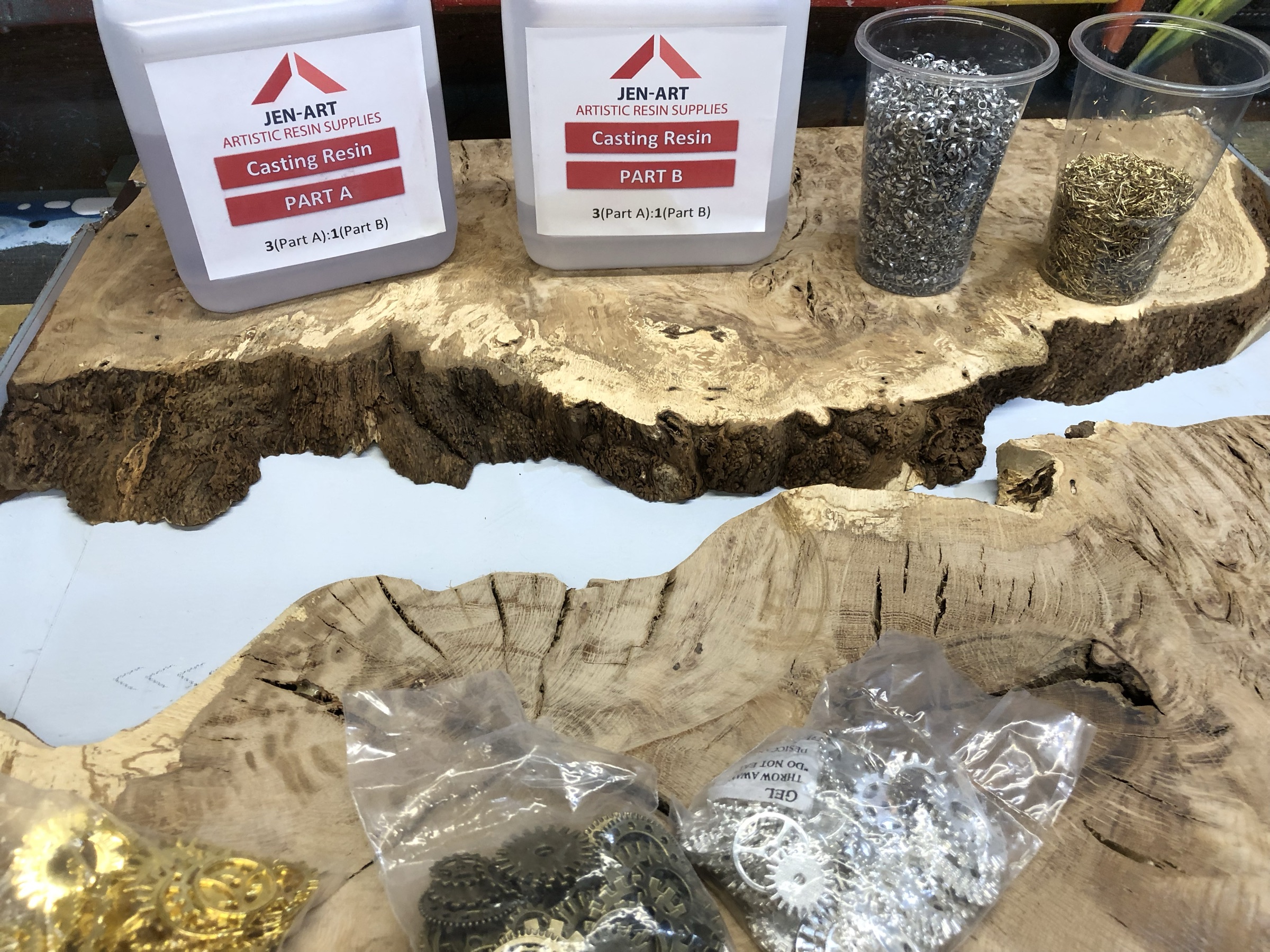 Casting resin and cups of metal shavings and gears laid out on the raw burl slabs, workshop