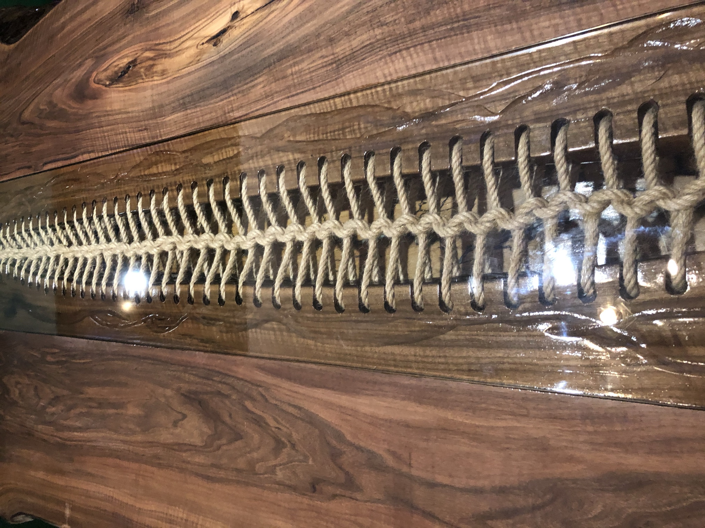 Macro detail of the hand-laced rope spine beneath a glossy clear channel, walnut grain either side