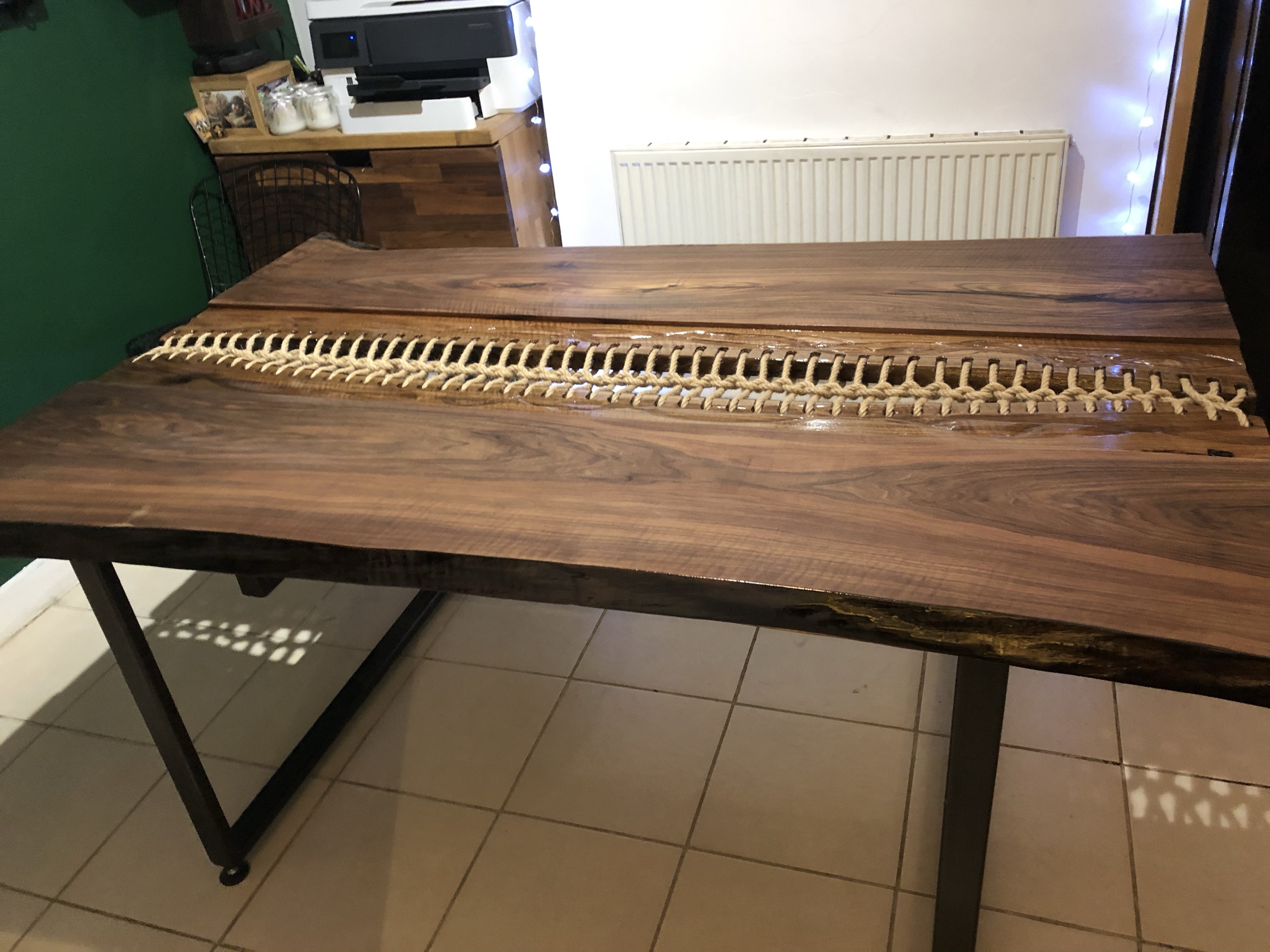 Walnut dining table with a rope-laced centre seam on black steel legs, indoor