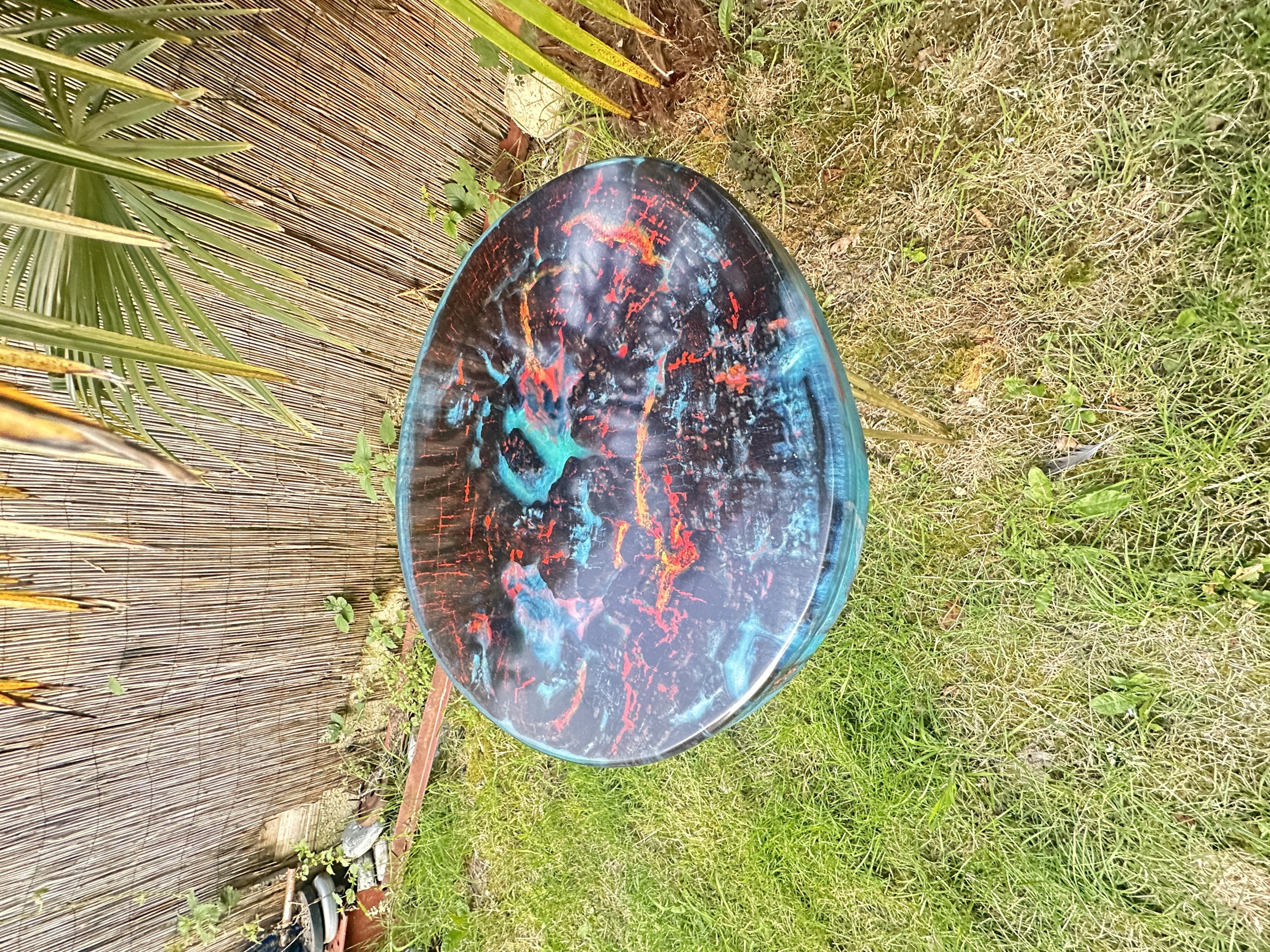 Round table with a charred timber top filled with red, orange and blue resin, outdoors