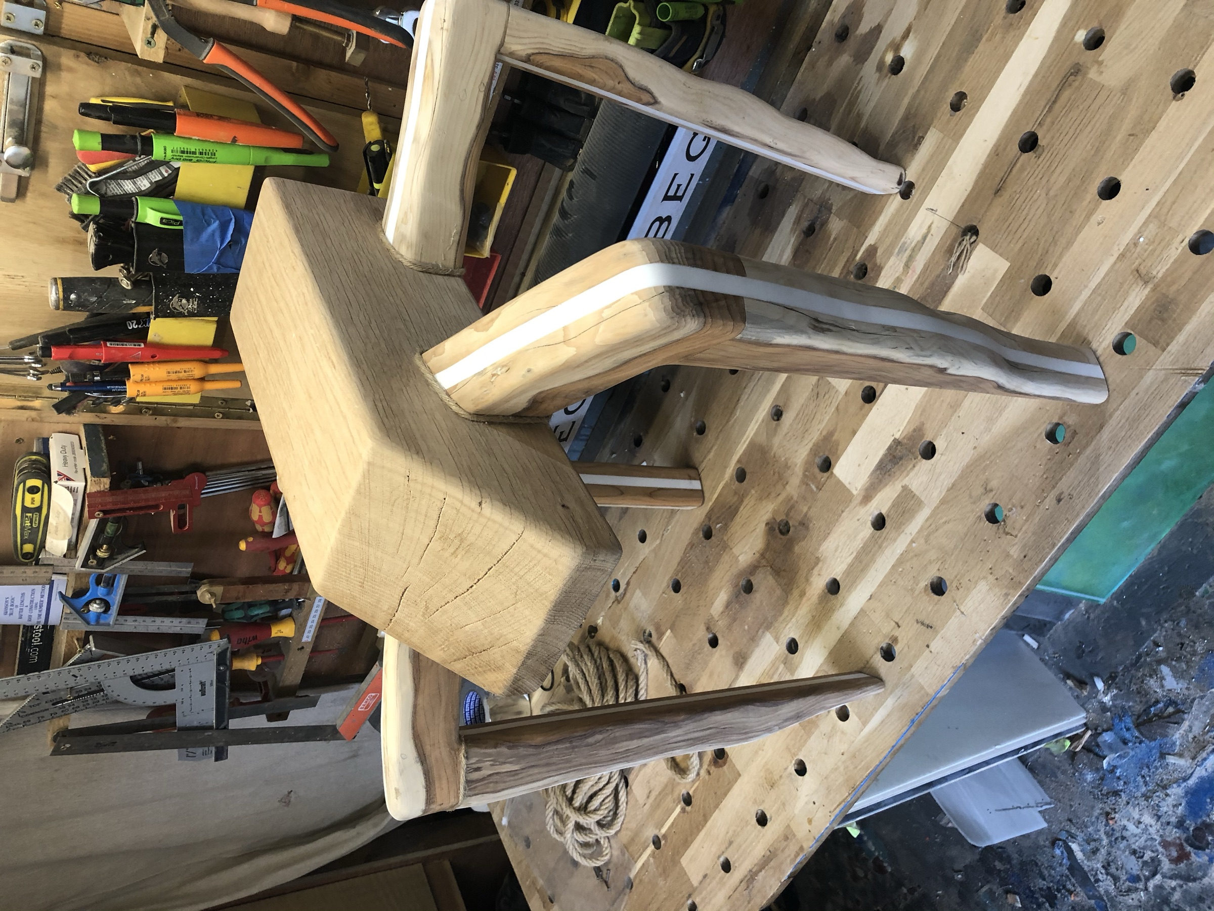 The carved legs joined to the raw top block early in construction, workshop pegboard behind